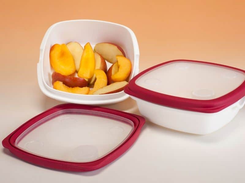 White tupperwares containing pieces of peach and apple inside